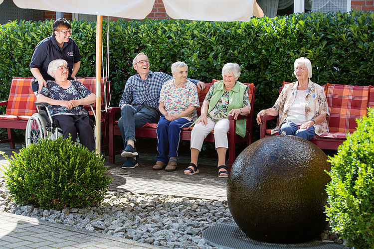 Mehrere Bewohner sitzen in geselliger Runde im Grünen und genießen die gemeinsame Zeit.