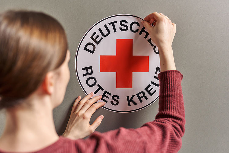 Symbolfoto Frau klebt ein DRK-Rundlogo an eine Wand