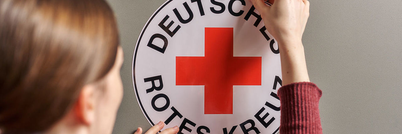 Symbolfoto Frau klebt ein DRK-Rundlogo an eine Wand
