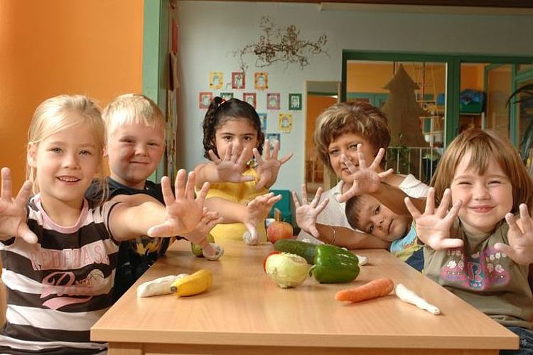 Kinder am Tisch, heben die Hände und lachen
