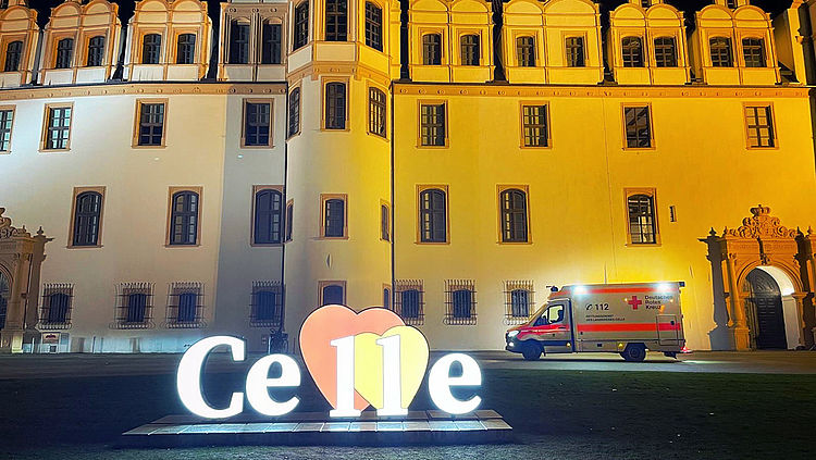 Leuchtendes Herz mit Celle-Schriftzug vor dem Celler Schloss am Abend. Dazwischen steht ein Rettungswagen, seitlich fotografiert.