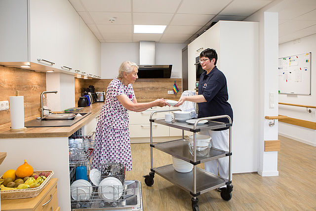 Pflegealltag mit Beteiligung: Eine Seniorin hilft beim Ausräumen der Geschirrspülmaschine.
