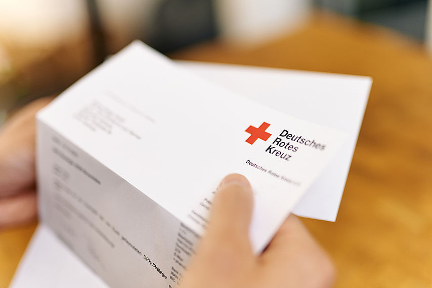 Symbolfoto Brief des DRK. Hand hält Briefbogen mit dem Logo.