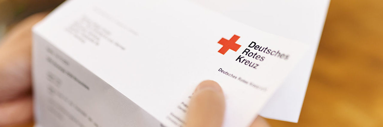 Symbolfoto Brief des DRK. Hand hält Briefbogen mit dem Logo.