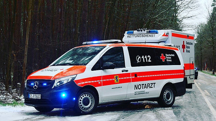 Ein Notarzteinsatzfahrzeug steht im Vordergrund auf einer schneebedeckten Fläche. Dahinter ist ein Rettungswagen zu sehen, beide Fahrzeuge sind schräg seitlich abgebildet.
