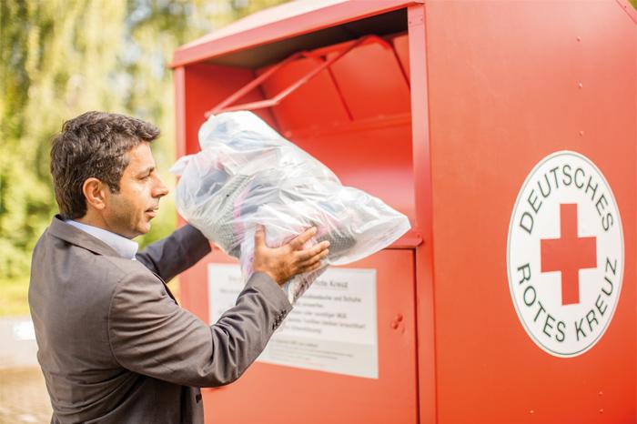 Kleidercontainer - ein Mann wirft einen Spendensack in einen roten Kleidercontainer