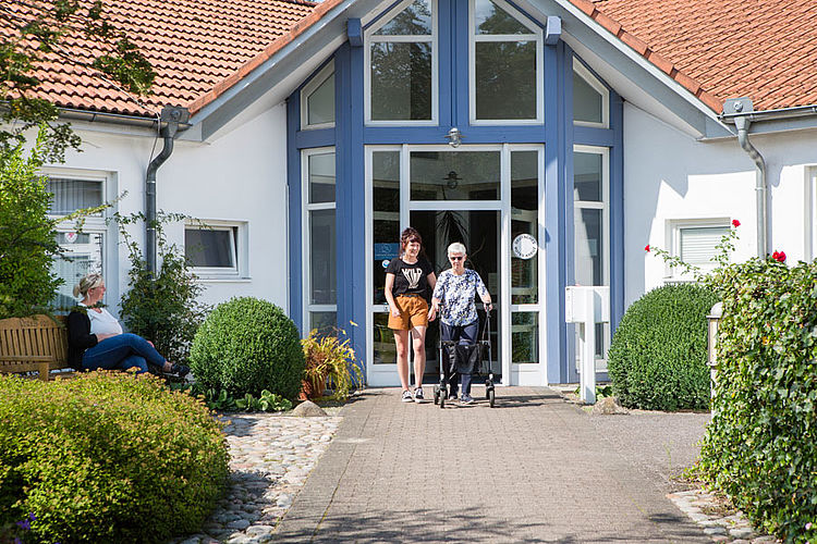 Begleitung mit Fürsorge – Betreuerin und Tagesgast stehen gemeinsam vor dem Eingang der Tagespflege.