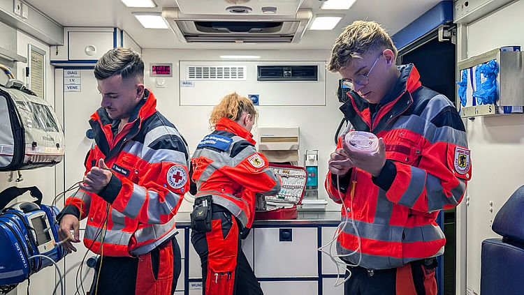 Drei Notfallsanitäter befinden sich im Inneren eines Rettungswagens und überprüfen medizinische Geräte – eine Szene aus dem Arbeitsalltag im Rettungsdienst.