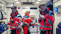 Drei Notfallsanitäter befinden sich im Inneren eines Rettungswagens und überprüfen medizinische Geräte – eine Szene aus dem Arbeitsalltag im Rettungsdienst.