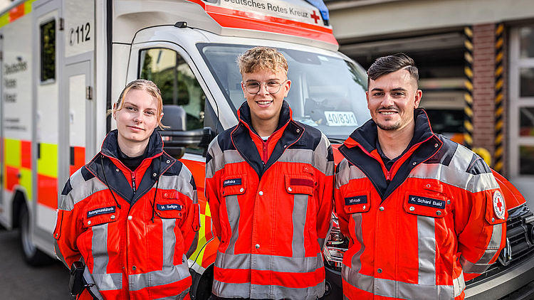 Drei junge Rettungsdienstkollegen stehen vor einem Rettungswagen