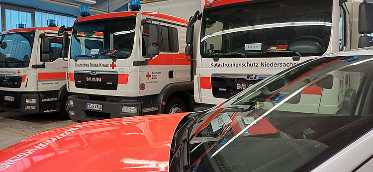 Innenansicht einer Fahrzeughalle mit Katastrophenschutzfahrzeugen, darunter auch mehrere Lkw für Transport und Versorgung.